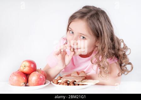 Kinder und Schokolade. Ein fröhliches Mädchen wählt zwischen Schokolade und Äpfeln. Gesunde Ernährung Stockfoto