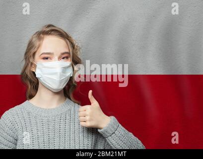 Glückliche Frau in Gesichtsmaske hält Daumen auf Polen Flagge Hintergrund. Konzept für Grippeepidemie und Virenschutz Stockfoto