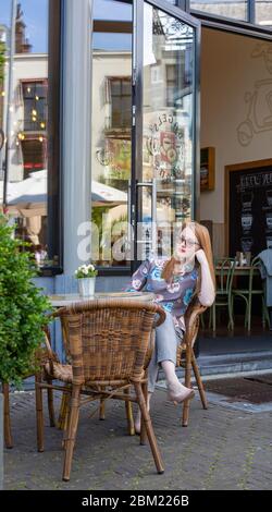 Junge Frau sitzt im Sommercafé auf der Straße in Den Haag, Niederlande und spricht per Telefon. Stockfoto