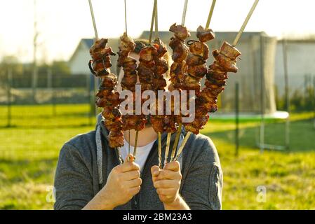 Hand mit Daumen nach oben hält Spieß mit Schaschlik. Mann hält Spieße mit vorbereitet Kebab. BBQ Stockfoto