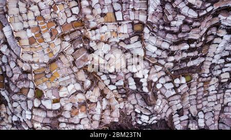 Luftaufnahme der Salzverdunstungsteiche in der Salzmine in Maras, Peru. Verschiedene Formen und Farben von Teichen schaffen das abstrakte Muster und die Form. Stockfoto