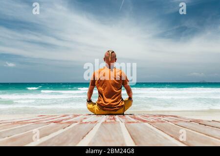 Der junge Mann sitzt am Ufer eines tropischen Strandes der Blick von hinten, der Ort der Meditation. Ein Panoramablick auf das Meer mit einem Sandstrand, auf einem Stockfoto