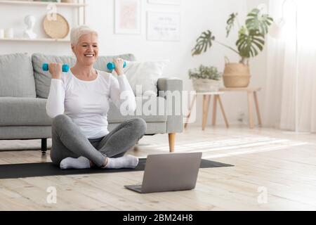 Aktive ältere Frau in Sportbekleidung mit Hanteln trainieren, Fitness zu Hause üben, leeren Raum Stockfoto