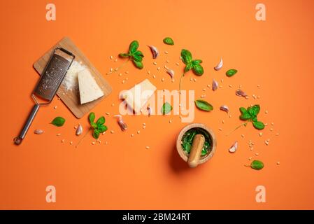 Herstellung von Pesto-Sauce mit frischem Basilikum, Parmesan, Knoblauch und Pinienkernen in einem Mörser mit Pestle, auf orangefarbenem Hintergrund. Die Zubereitung von Pesto Stockfoto