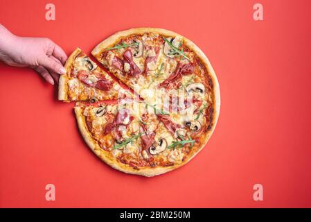 Flach liegend mit einer jungen Frau Hand, die ein Stück Pizza greift. Hausgemachte Pizza mit Prosciutto crudo und Rucola. Leckere Schinkenpizza. Stockfoto