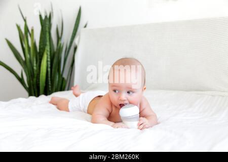 Schönes Baby, das Milch aus der Flasche im weißen Schlafzimmer isst Weißer Hintergrund Stockfoto