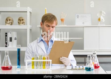 Ein junger brasilianischer Wissenschaftler notiert die Ergebnisse seiner chemischen Verbindungen Forschung auf dem Clipboard. Arbeitsatmosphäre im chemischen Labor. Reagenzglas Stockfoto