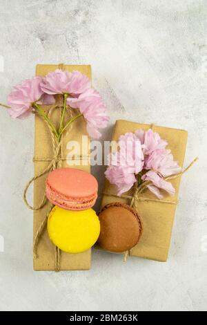 Mehrfarbige Makronen mit Pfingstrosen und Geschenkbox auf grauem Marmortisch. Draufsicht, Nahaufnahme Stockfoto