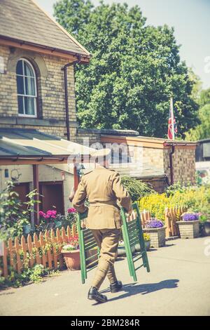 1940er Jahre WKII Großbritannien Ereignis, Severn Valley Railway, Großbritannien. Mann in militärischer Uiniform trägt Stühle. Stockfoto