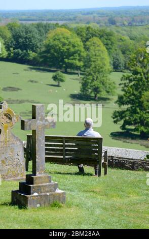 Boughton Monchelsea Village, Kent, Großbritannien. Mann auf einer Bank im Hof der St. Peter Kirche mit Blick auf den Hirschpark am Kentish Weald Stockfoto