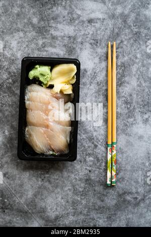 Zum Mitnehmen Suzuki Fisch Sashimi mit eingelegtem Ingwer und Wasabi in schwarzem Kunststoff-Teller-Container / Paket. Traditionelles Fast Food. Bereit zum Essen. Stockfoto