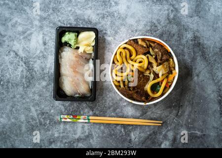 Take Away Asian Food Menu Set mit Beef Udon Nudelsuppe und Raw Suzuki Fish Sashimi serviert mit eingelegtem Ingwer und Wasabi. Stockfoto