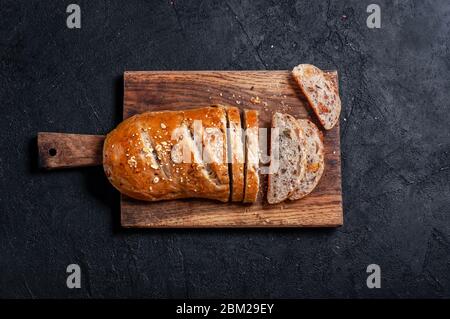 Hausgemachtes Mehrkornbrot in Scheiben geschnitten mit Leinsamen und Sesam auf Holzbrett auf dunklem Tisch. Draufsicht Flaches Lay Stockfoto