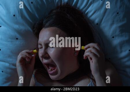 Junge Frau, die Ohrenstöpsel in ihre Ohren für die Lärmreduzierung vor dem Schlaf, Schlaflosigkeit Stockfoto