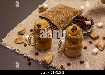 Dalgona Kaffee im Einmachglas. Koreanischer flauschiger Schlagkaffee. Trendiges Quarantänegetränk, Zucker und Kaffeebohnen auf schwarzem Steinbeton-Hintergrund Stockfoto