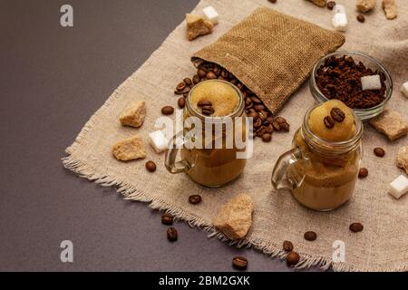 Dalgona Kaffee im Einmachglas. Koreanischer flauschiger Schlagkaffee. Trendiges Quarantänegetränk, Zucker und Kaffeebohnen auf schwarzem Steinbeton-Hintergrund Stockfoto