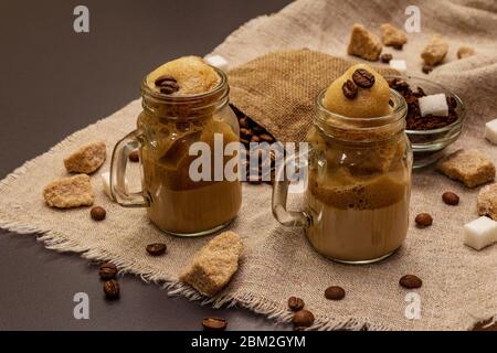 Dalgona Kaffee im Einmachglas. Koreanischer flauschiger Schlagkaffee. Trendiges Quarantänegetränk, Zucker und Kaffeebohnen auf schwarzem Steinbeton-Hintergrund Stockfoto