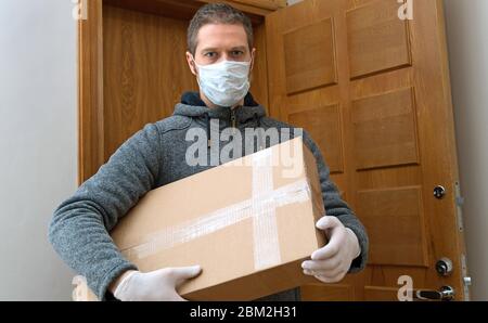 Männlicher Kurier in medizinischer Maske und Handschuhe mit Paket. Stockfoto