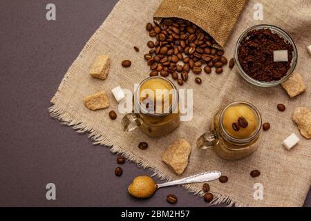 Dalgona Kaffee im Einmachglas. Koreanischer flauschiger Schlagkaffee. Trendiges Quarantänegetränk, Zucker und Kaffeebohnen auf schwarzem Steinbeton-Hintergrund Stockfoto