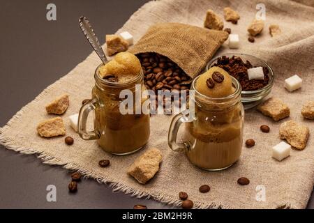 Dalgona Kaffee im Einmachglas. Koreanischer flauschiger Schlagkaffee. Trendiges Quarantänegetränk, Zucker und Kaffeebohnen auf schwarzem Steinbeton-Hintergrund Stockfoto