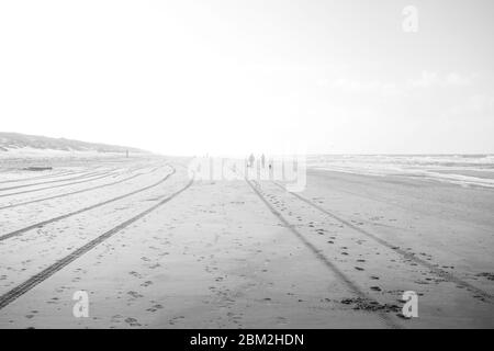 Spuren im Sand führen den Blick zum Horizont. Dort kann man Wanderer sehen. Der Sand ist durch Wanderungen und Gassen gekennzeichnet. Schwarzweiß-Fotografie. Stockfoto