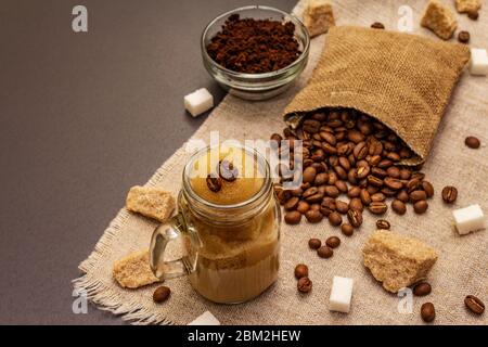 Dalgona Kaffee im Einmachglas. Koreanischer flauschiger Schlagkaffee. Trendiges Quarantänegetränk, Zucker und Kaffeebohnen auf schwarzem Steinbeton-Hintergrund Stockfoto