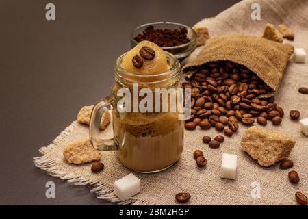 Dalgona Kaffee im Einmachglas. Koreanischer flauschiger Schlagkaffee. Trendiges Quarantänegetränk, Zucker und Kaffeebohnen auf schwarzem Steinbeton-Hintergrund Stockfoto