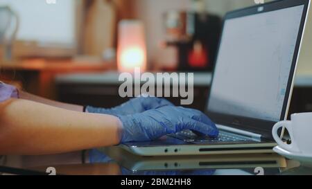 Nahaufnahme von Frauenhände in medizinischen Handschuhen, die auf der Tastatur tippen. Im Hintergrund warme Lichter. Stockfoto