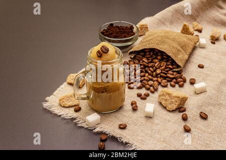 Dalgona Kaffee im Einmachglas. Koreanischer flauschiger Schlagkaffee. Trendiges Quarantänegetränk, Zucker und Kaffeebohnen auf schwarzem Steinbeton-Hintergrund Stockfoto
