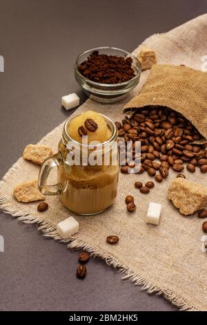 Dalgona Kaffee im Einmachglas. Koreanischer flauschiger Schlagkaffee. Trendiges Quarantänegetränk, Zucker und Kaffeebohnen auf schwarzem Steinbeton-Hintergrund Stockfoto