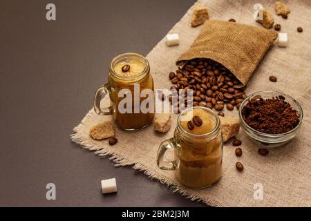 Dalgona Kaffee im Einmachglas. Koreanischer flauschiger Schlagkaffee. Trendiges Quarantänegetränk, Zucker und Kaffeebohnen auf schwarzem Steinbeton-Hintergrund Stockfoto