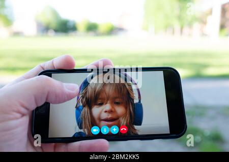 Vater und Tochter sprechen miteinander durch einen Videoanruf auf einem Smartphone - Hand hält ein Smartphone mit einem kleinen Mädchengesicht - Distanz Beziehung Stockfoto