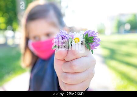 Kleines nettes Mädchen mit Schutzmaske hält Bündel von Wildblumen - Nahaufnahme auf der Hand mit Geschenk an Mama - Wildblumen in der geballten Faust Stockfoto