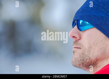 Nahaufnahme Von Kaukasischen Männlichen Trägt Sonnenbrille Und Hut Im Winter. Seine Sonnenbrille Zeigt Die Reflexion Der Winterlandschaft Im Wald. Stockfoto
