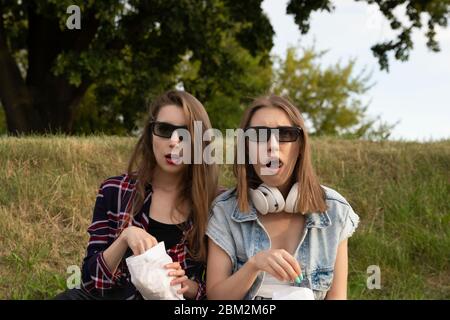 Zwei Mädchen sitzen im Park direkt auf dem Gras und essen Popcorn. Freundinnen schauen sich einen Film in einem Outdoor Kino an. Stockfoto