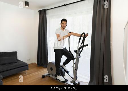 Ein Mann geht in Quarantäne zu Hause zum Sport. Ein junger Mann wird auf einem Simulator engagiert, ohne nach draußen zu gehen. Stockfoto
