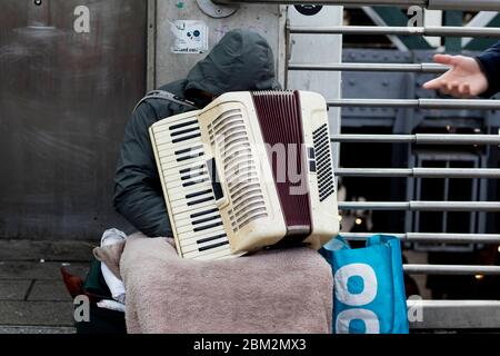 London, UK - 23. Februar 2020 unkenntlich gebeugt sich der rumänische Straßenmusiker während der Ruhepause den Kopf auf einer Ziehharmonika Stockfoto