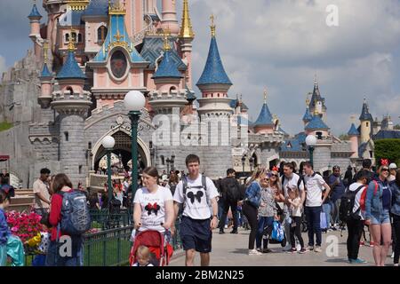 Auf einer Straße eines Themenparks inmitten einer Menschenmenge stehend. Wanderbesucher im Freizeitpark vor einem süßen Schloss mit bewölktem Himmel. Paris F Stockfoto