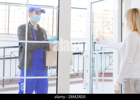 Kurier in Schutzmaske liefert Paket, Kunde in medizinischen Handschuhen erhält Box. Lieferservice unter Quarantäne, Krankheitsausbruch, Coronavirus Stockfoto