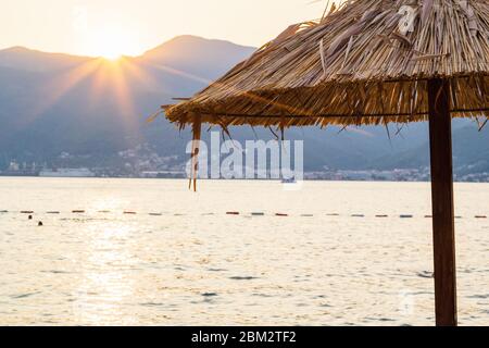 Stroh Sonnenschirm am Strand in Montenegro und schönen Sonnenuntergang hinter den Bergen Stockfoto