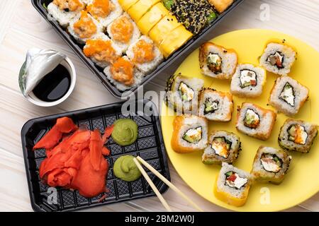 Sushi, rohes Gemüse, eingewickelt in Algen. Brötchen auf gelbem Teller mit Wasabi und Sojasoße auf Holzbrett Hintergrund. Ein japanisches Gericht mit Meeresfrüchten und Lch Stockfoto