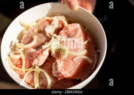 Rohes Rindfleisch Fleisch in Marinade. Rohes Fleisch Schweinefleisch oder Rindfleisch in einem Teller in männlicher Hand, Vorbereitung gesunder Lebensmittel, Marinade und Gewürze Paprika, Menü Konzept Hintergrund Stockfoto
