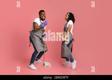 Fröhliches Housekeeping Konzept. Fröhlich Afrikanischen Paar Von Reinigungsmaschinen Mit Spaß Während Der Hausarbeiten Stockfoto