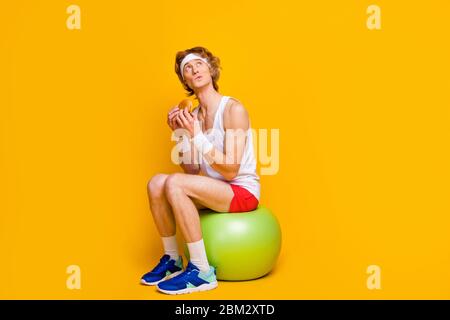 Porträt von seinem er schön attraktiv funky sportlich Kerl sitzt auf fitball Essen lecker lecker lecker Essen Zählen Kalorien isoliert über helle lebendige Glanz Stockfoto