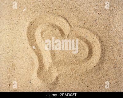 Herz mit einem Finger auf einem trockenen gelben Meersand gezeichnet. Konzept der Liebe, Sonne, heißen Sommer, Urlaub am Meer und Urlaub am Strand. Draufsicht. Stockfoto