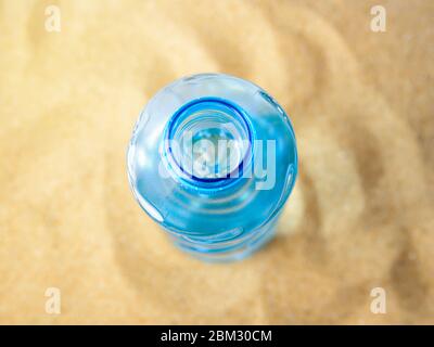 Offene blaue Plastikflasche mit Trinkwasser auf einem gelben Meersand. Konzept von Durst, heißen Sommerwetter, Urlaub am Meer und Urlaub am Strand. Stockfoto