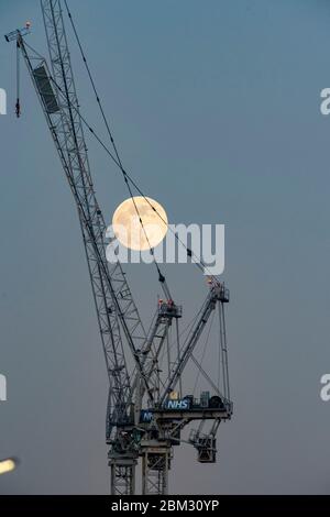 Brighton UK 6. Mai 2020 - der dritte und letzte Supermond des Jahres, bekannt als der Blumenmond, steigt hinter einem NHS-Krankenhauskran auf, der während der Coronavirus COVID-19 Pandemiekrise an der Erweiterung des Royal Sussex County Hospital in Brighton arbeitet. . Quelle: Simon Dack / Alamy Live News Stockfoto