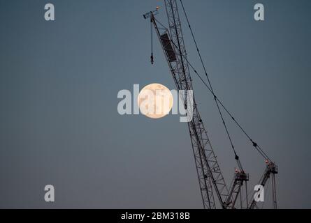 Brighton UK 6. Mai 2020 - der dritte und letzte Supermond des Jahres, bekannt als der Blumenmond, steigt hinter einem NHS-Krankenhauskran auf, der während der Coronavirus COVID-19 Pandemiekrise an der Erweiterung des Royal Sussex County Hospital in Brighton arbeitet. . Quelle: Simon Dack / Alamy Live News Stockfoto