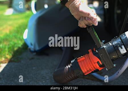 Hand Dumping RV Tank Ventil, um grau grau schwarz Abwasser und Abwasser freizugeben, während auf dem Campingplatz Dump Station geparkt. Kajak liegt im Hintergrund. Stockfoto