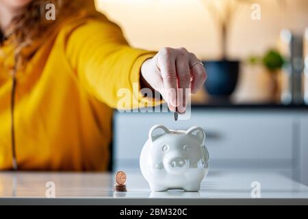 Persönliche Finanzen, Frau, die Geld in ein Sparschwein- -Reichtum und Finanzkonzept. Weißes Sparschwein im Vordergrund. Stockfoto